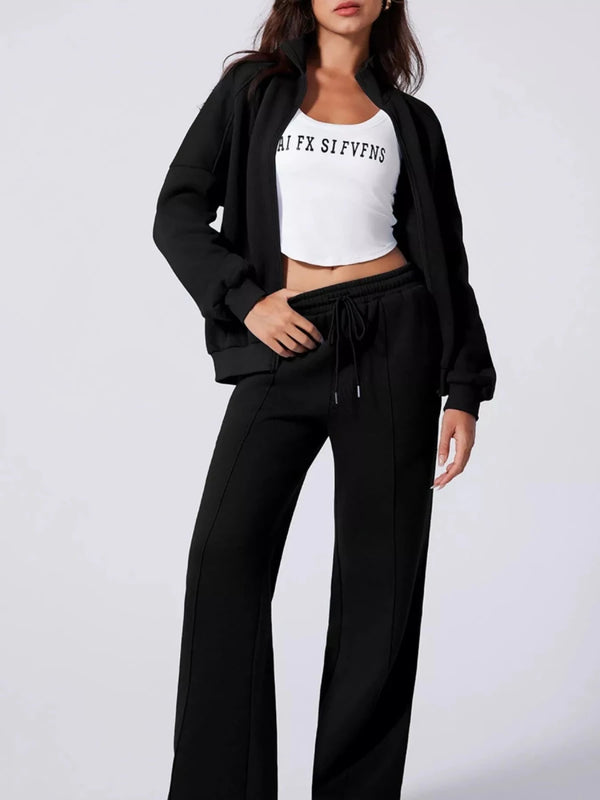 Woman wearing a black tracksuit with a white crop top on a light gray background