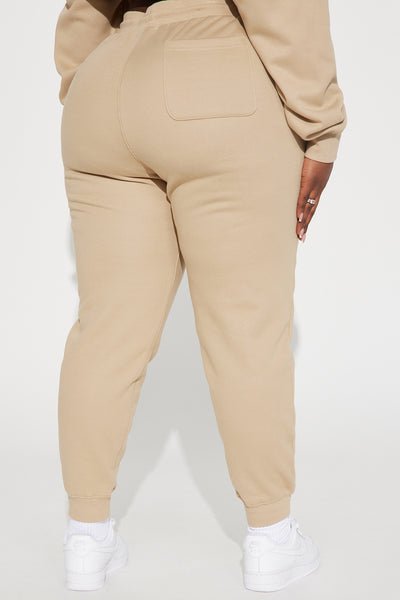 A person shown from the back wearing beige jogger sweatpants with a back pocket, a matching beige sweatshirt, and white sneakers against a plain light background.