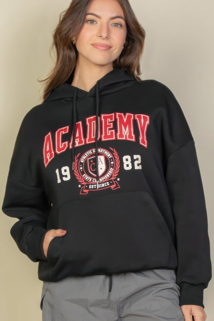 Person wearing a black hoodie with 'Academy' and '1982' text on a beige background