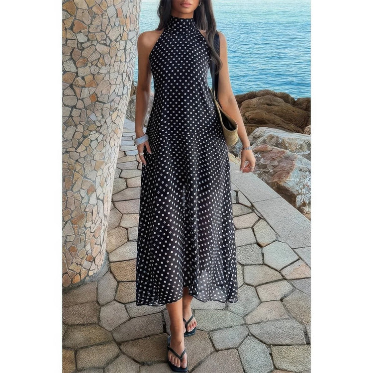 Woman in a black polka dot dress standing by a stone wall with ocean view