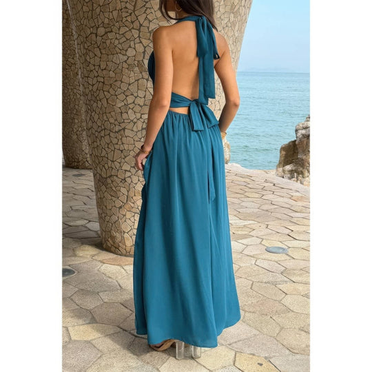 Woman wearing a blue dress with a stone wall and ocean view in the background