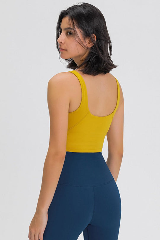 Woman wearing a yellow tank top and blue leggings on a white background