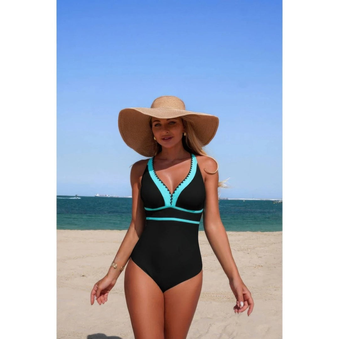 Woman in a black and teal swimsuit with a wide-brimmed hat on a beach.