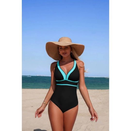 Woman in a black and teal swimsuit with a wide-brimmed hat on a beach.