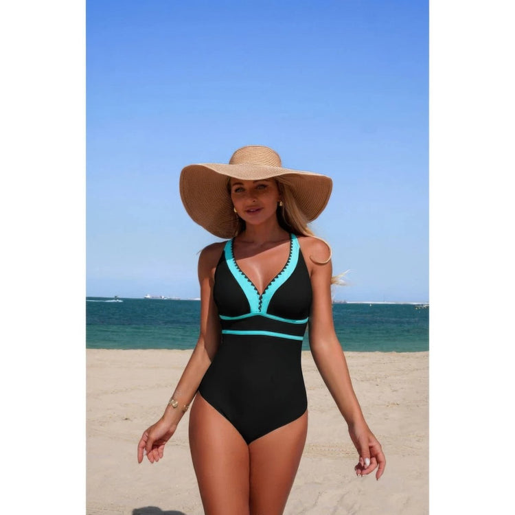 Woman in a black and teal swimsuit with a wide-brimmed hat on a beach.