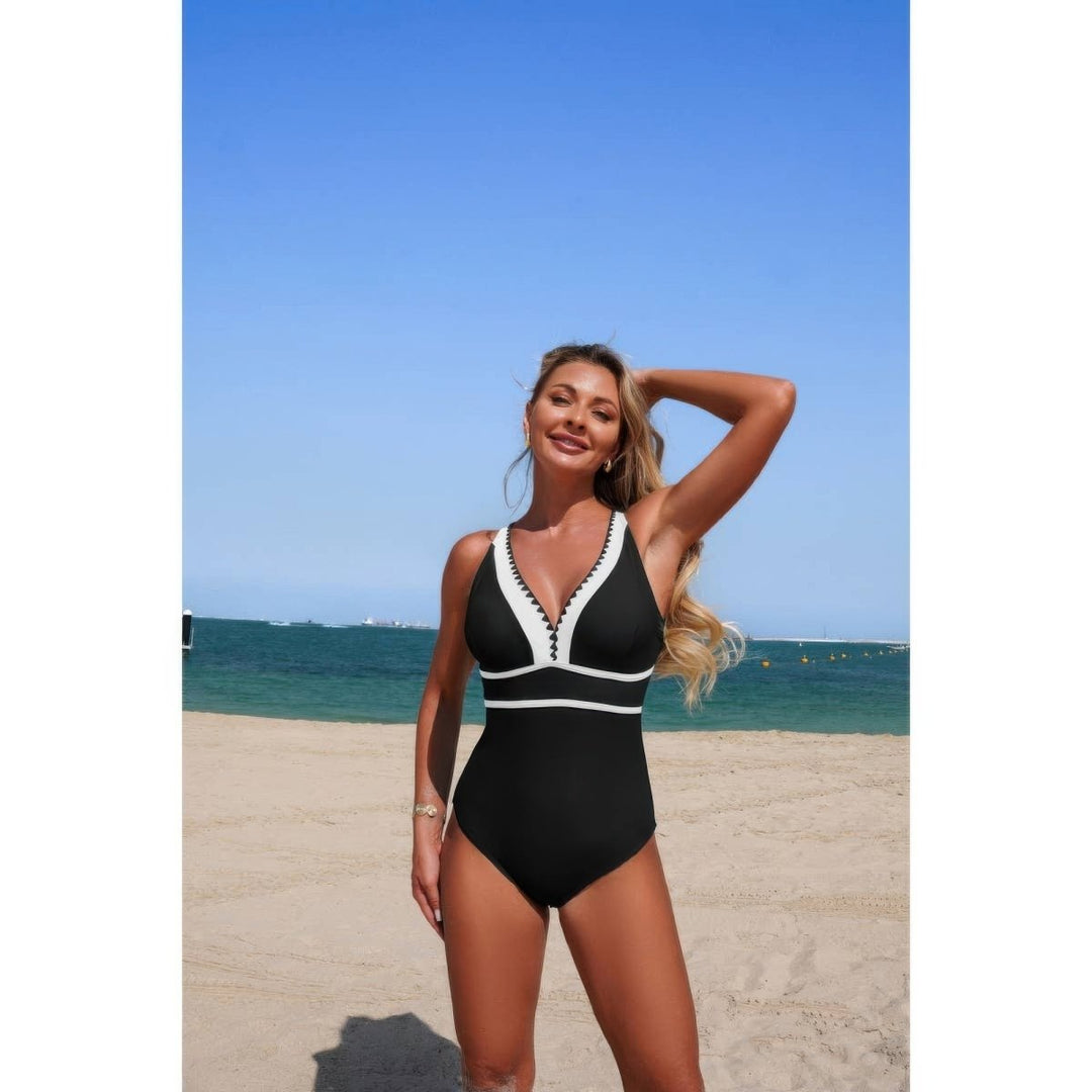 Woman in a black and white swimsuit standing on a beach with clear blue sky and ocean.