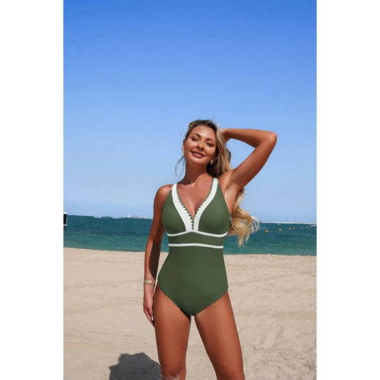 Woman in a green swimsuit standing on a beach with clear blue sky and ocean.