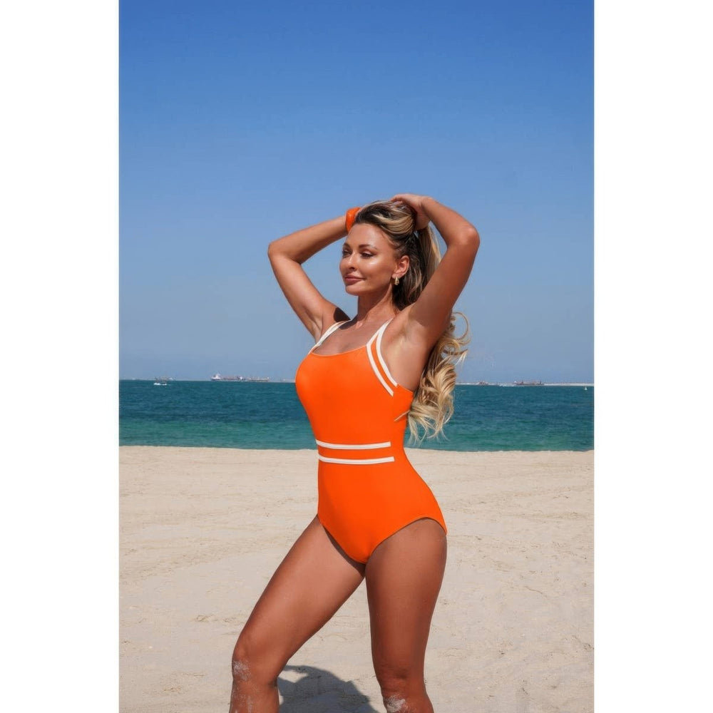 Woman in an orange swimsuit standing on a beach with clear blue sky and ocean.