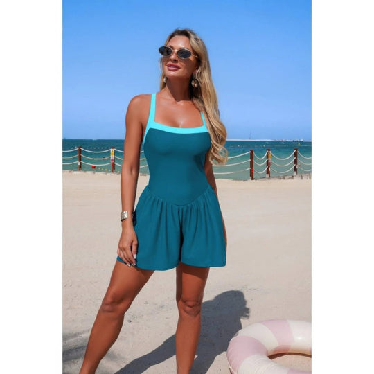 Woman in a teal swimsuit standing on a beach with ocean view