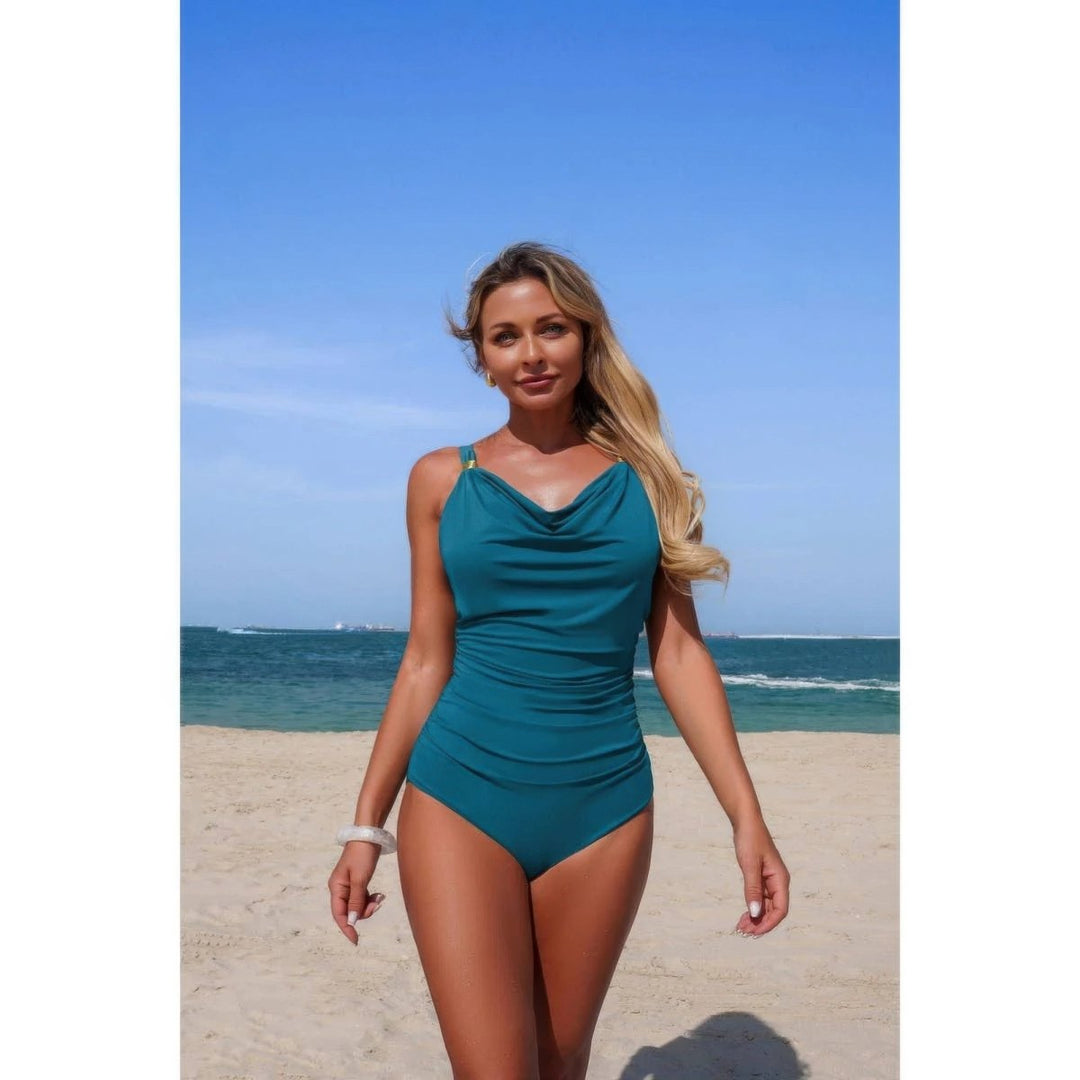 Woman in a teal swimsuit standing on a beach with ocean and clear sky in the background