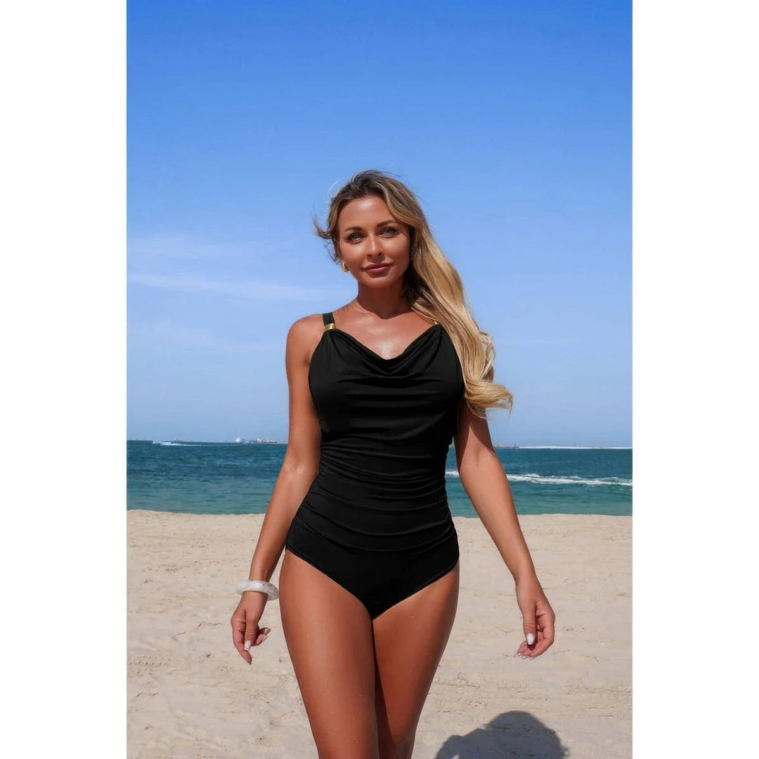 Woman in a black swimsuit standing on a beach with blue sky and ocean in the background