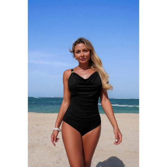 Woman in a black swimsuit standing on a beach with blue sky and ocean in the background