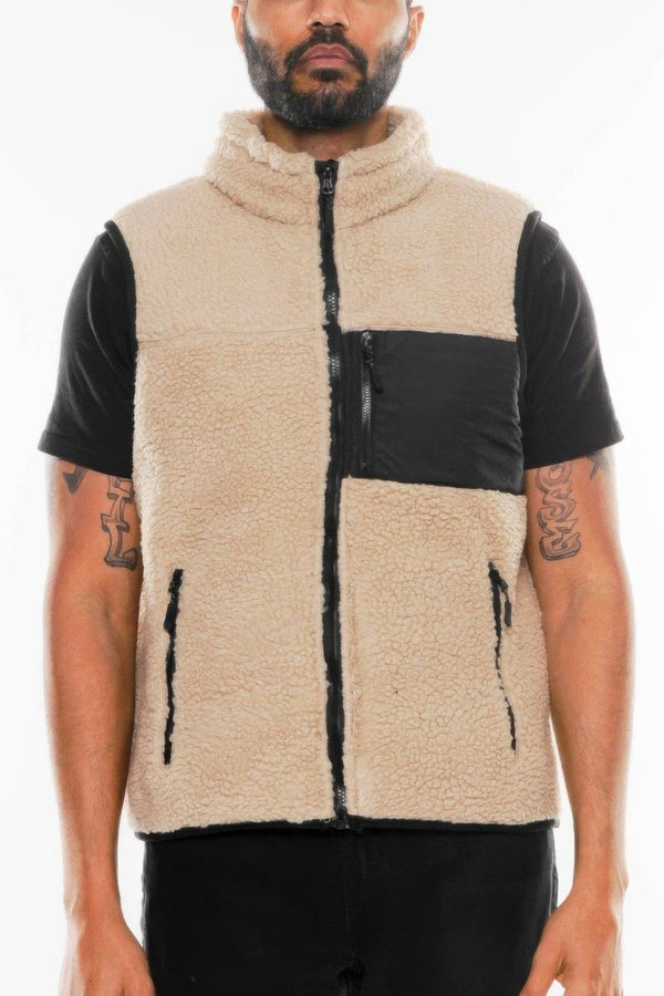 Man wearing a beige fleece vest with black accents on a white background