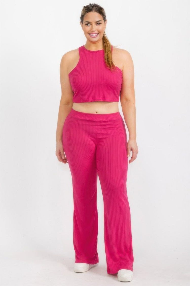 A woman modeling a bright pink ribbed two-piece set consisting of a sleeveless halter crop top and matching wide-leg pants, photographed against a plain light gray studio background.