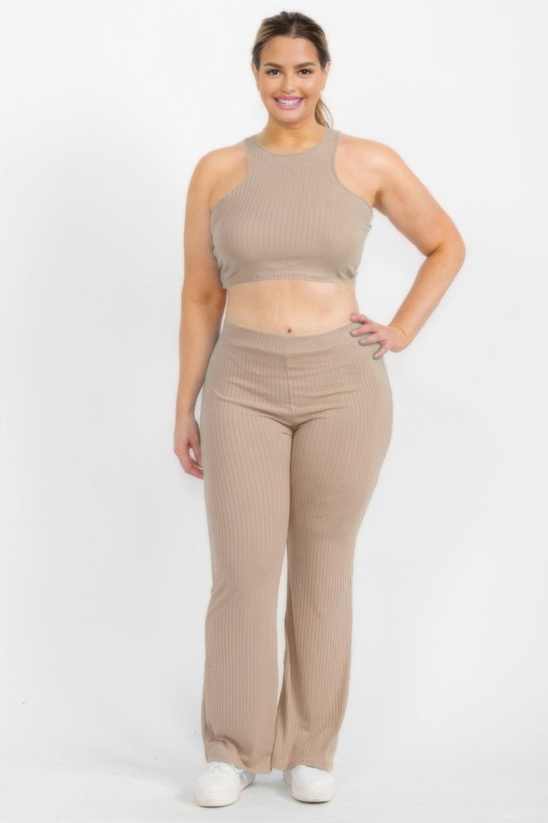 A woman modeling a matching ribbed two-piece set consisting of a beige halter crop top and high-waisted flared pants, paired with white sneakers against a plain white studio background.