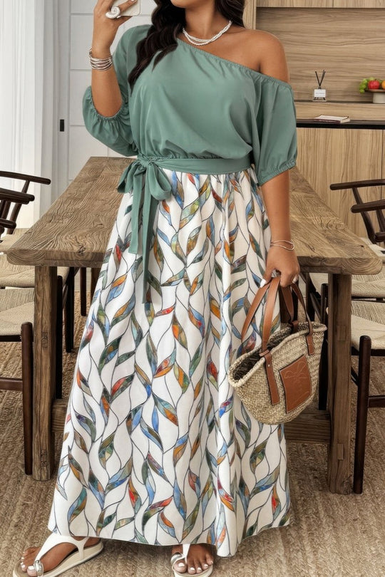 Woman in a green off-shoulder top and patterned skirt standing in a dining area.