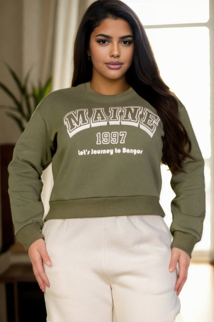 Woman wearing a green sweatshirt with 'MAINE 1997' text, standing indoors.