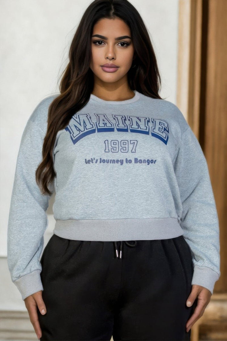Woman wearing a gray sweatshirt with 'MAINE 1997' text, standing indoors.