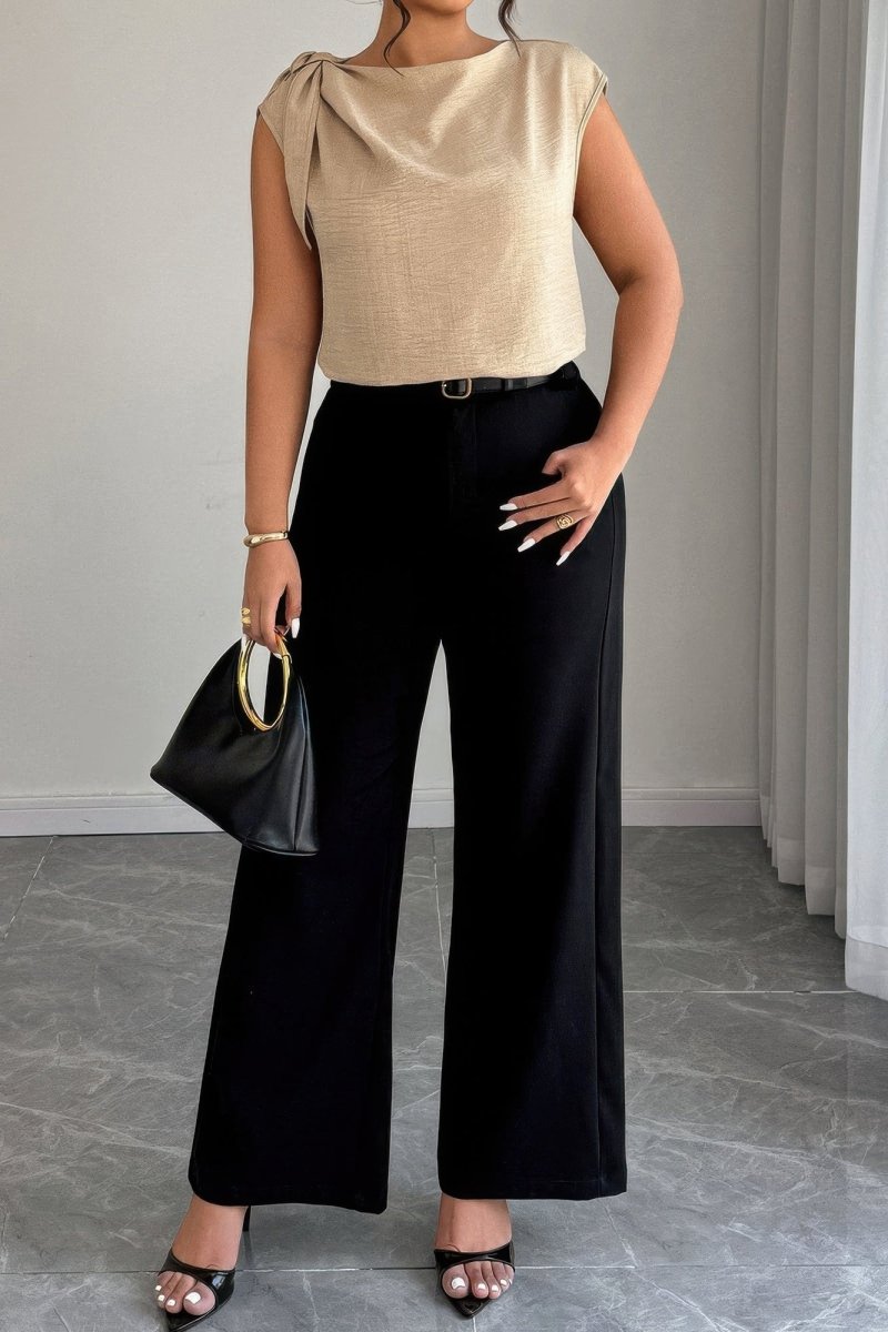 Woman wearing a beige top and black pants holding a black handbag indoors.