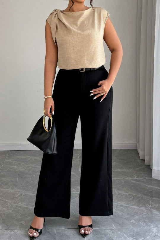 Woman wearing a beige top and black pants holding a black handbag indoors.