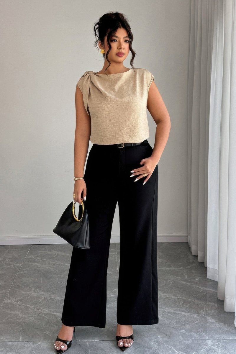 Woman wearing a beige top and black pants with a handbag indoors.