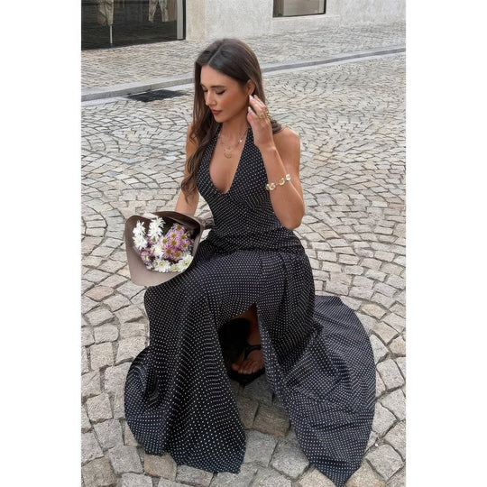 Woman in a black polka dot dress sitting on a cobblestone street holding flowers.