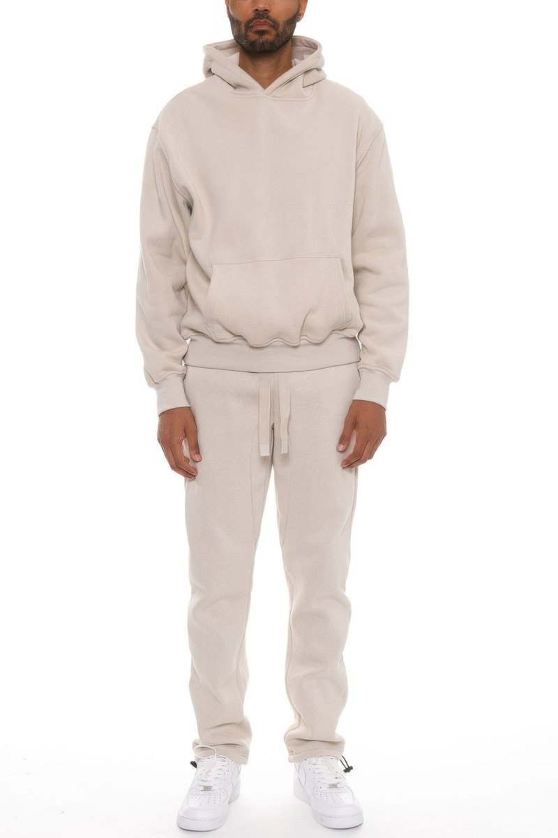 A man modeling a matching beige hoodie and sweatpants set with white sneakers, shot against a plain white background.