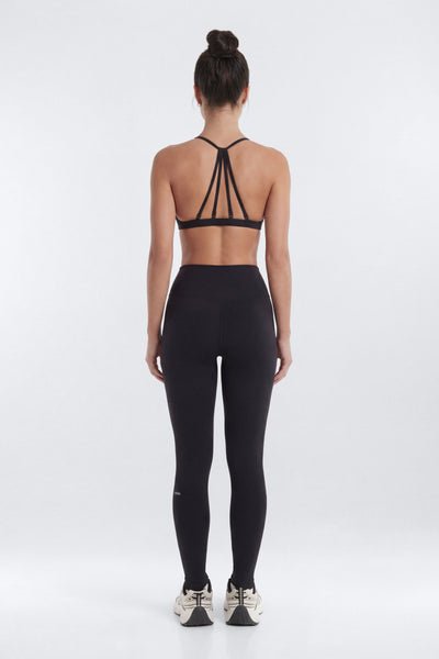 Person wearing a black strappy top and leggings on a white background