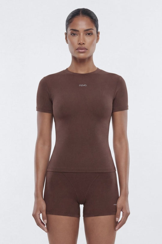 A model wearing a matching brown short-sleeve top and shorts set with a small white logo on the chest, photographed against a light gray studio background.