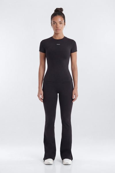 A woman modeling a black short-sleeve athletic top and matching black flared pants against a light gray studio background.