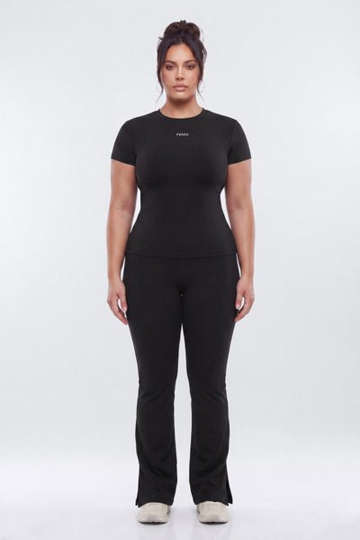 A woman modeling a black short-sleeve athletic top and matching black pants against a light gray studio background.