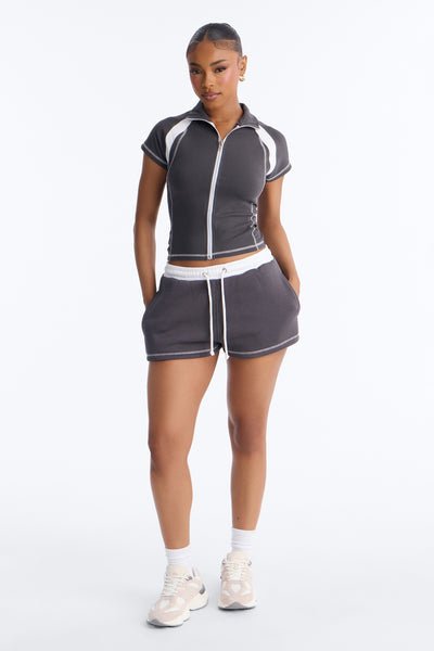 Woman wearing a gray athletic outfit with white accents on a white background