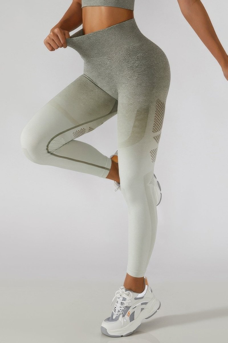 A model wearing high-waisted athletic leggings with a gray-to-white ombre gradient and textured side panels, paired with white sneakers, against a light gray studio background.