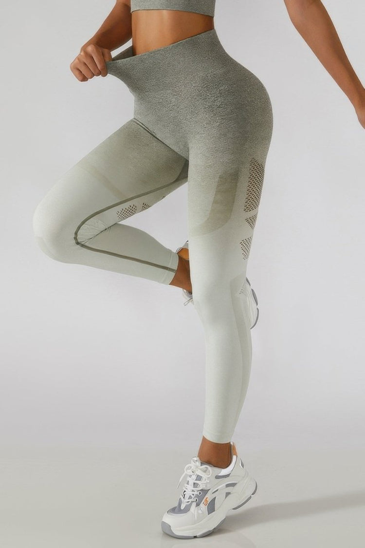 A model wearing high-waisted athletic leggings with a gray-to-white ombre gradient and textured side panels, paired with white sneakers, against a light gray studio background.