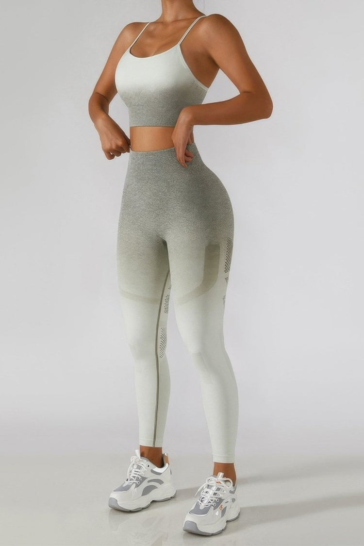 A woman modeling a matching two-piece activewear set consisting of a light gray sports bra and high-waisted leggings with a gradient fade to off-white, paired with white and gray sneakers, against a plain light gray studio background.