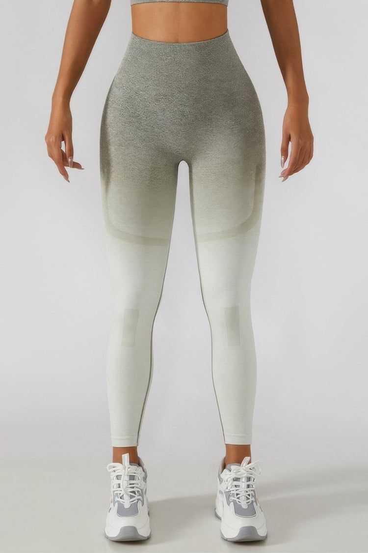 A model from the waist down wearing high-waisted gradient leggings that fade from heather gray at the top to off-white at the bottom, paired with white and gray sneakers.