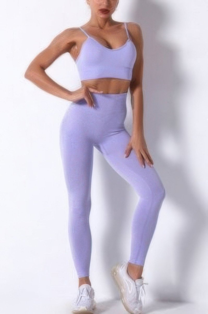 A woman modeling a matching lavender-purple activewear set consisting of a sports bra and high-waisted leggings, paired with white sneakers, against a plain white studio background.