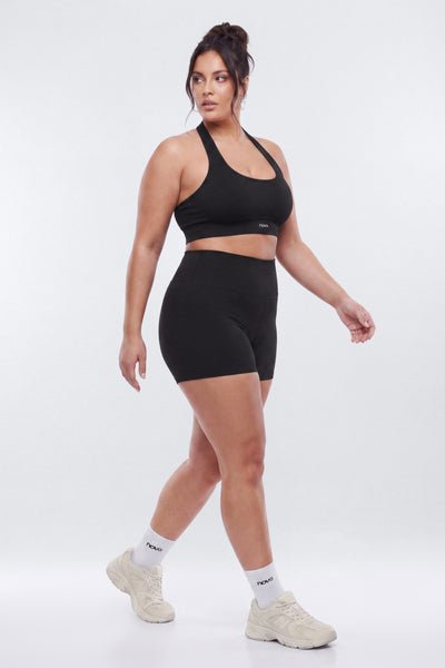 Woman wearing a black sports bra and shorts set on a white background