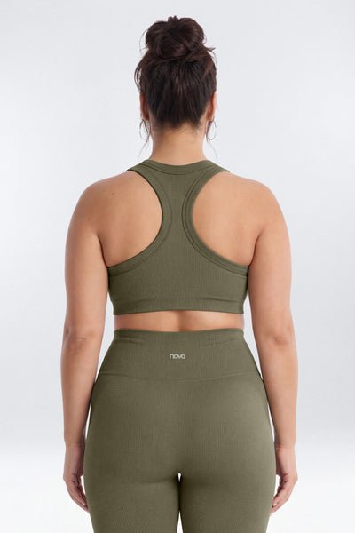 A woman viewed from the back wearing an olive green sports bra and matching high-waisted leggings against a light gray studio background.