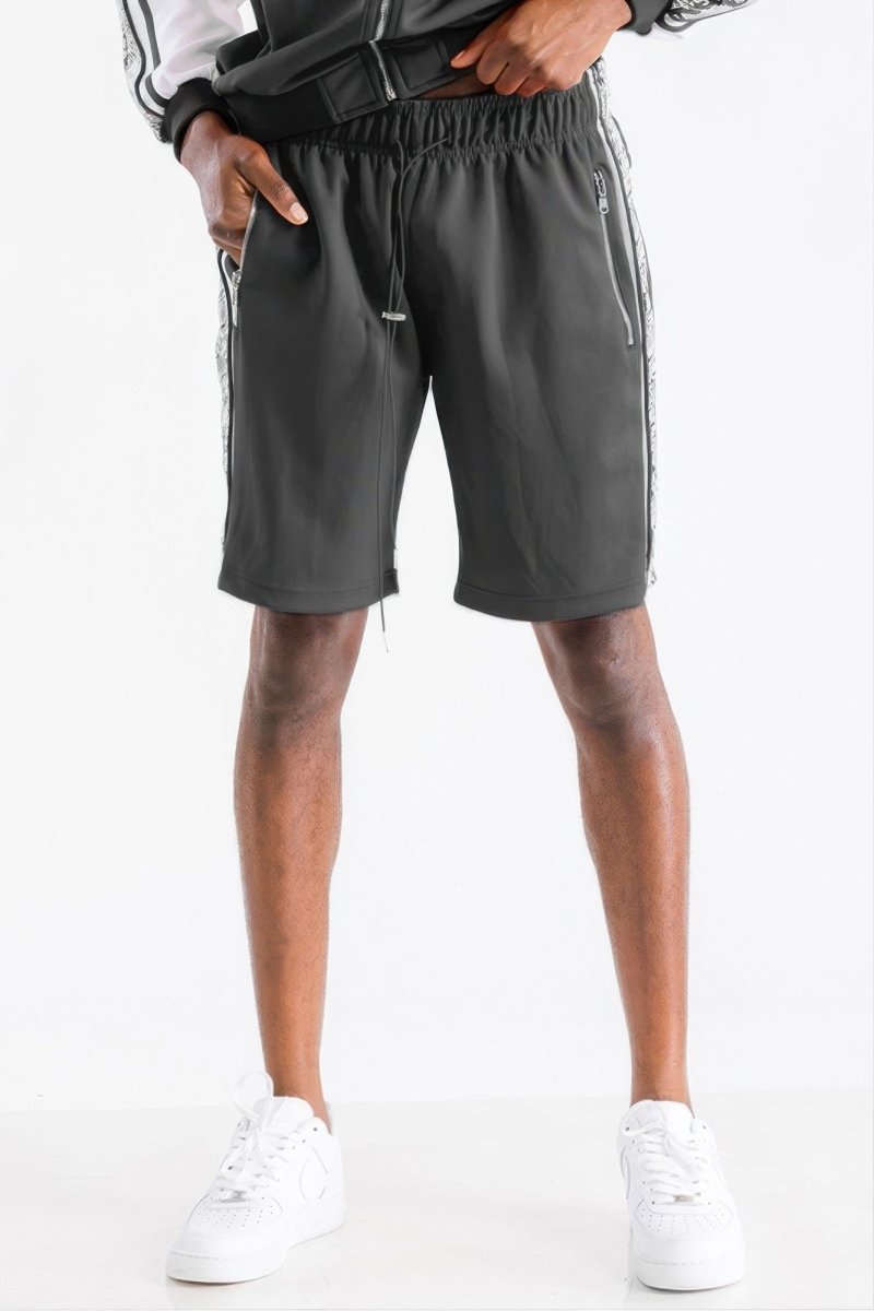 A person wearing dark gray athletic shorts with white side stripes, paired with a black and white jacket and white sneakers, shown from the waist down against a plain white background.