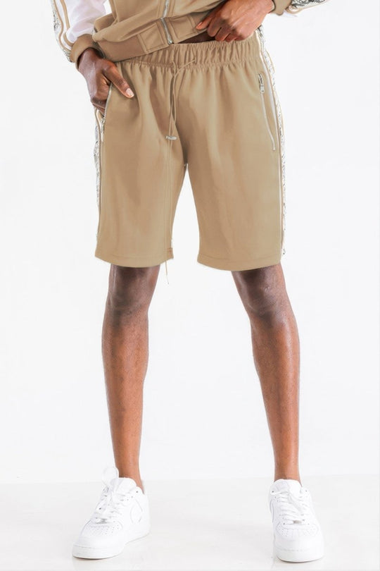 A person wearing beige athletic shorts with white side stripes, paired with a matching beige top and white sneakers, shown from the waist down against a plain white background.