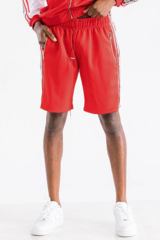 A person wearing bright red athletic shorts with white side stripes, paired with a matching red and white top and white sneakers, shown against a plain white studio background.
