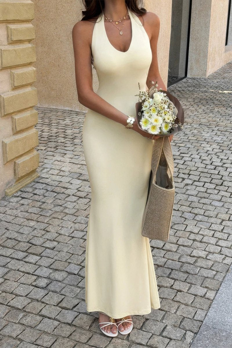 Woman in a long light-colored dress holding flowers on a cobblestone street.