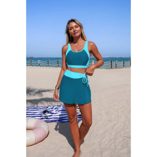 Woman in teal sports outfit standing on a beach with ocean view
