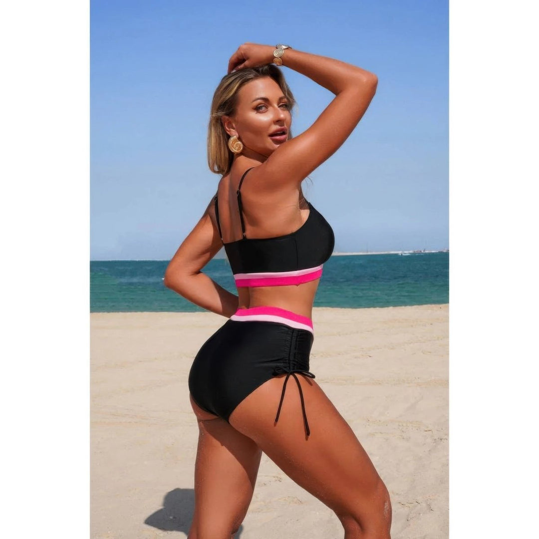Woman in a black and pink bikini standing on a beach with blue sky and ocean in the background