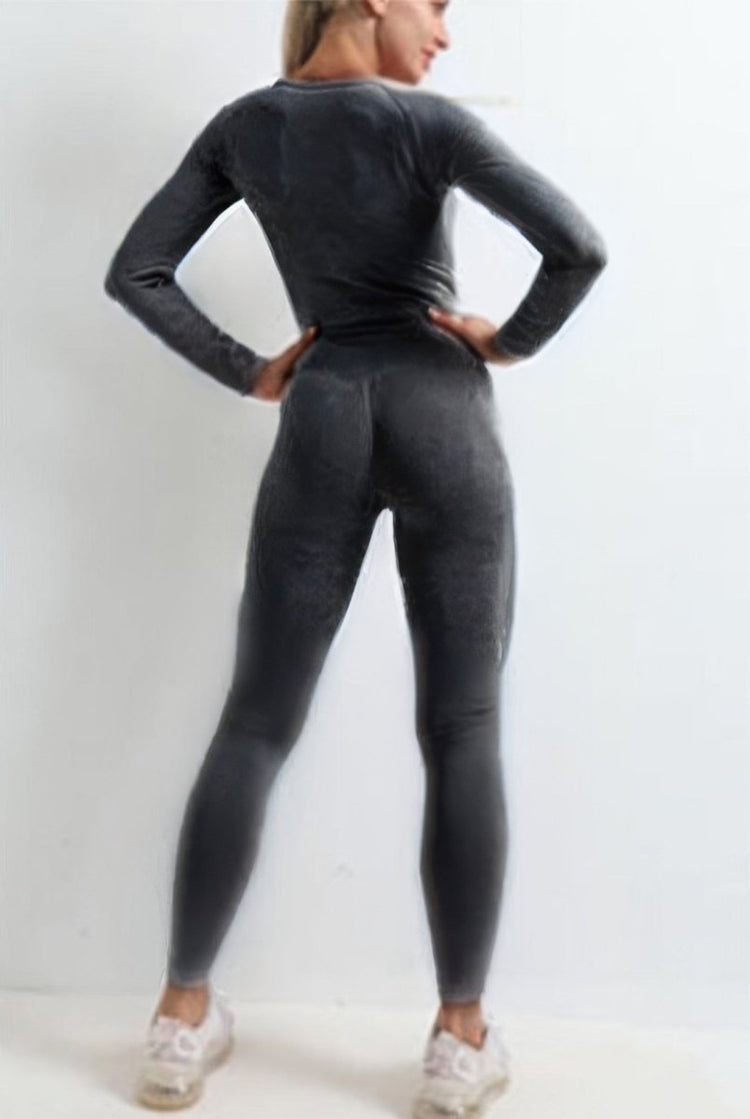 A woman wearing a dark gray long-sleeve athletic top and matching high-waisted leggings, shown from the back against a plain white studio background.