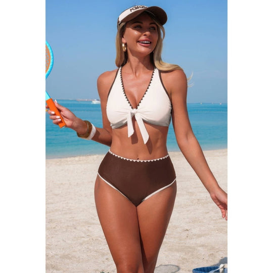 Woman in a two-tone swimsuit holding a tennis racket on a beach.