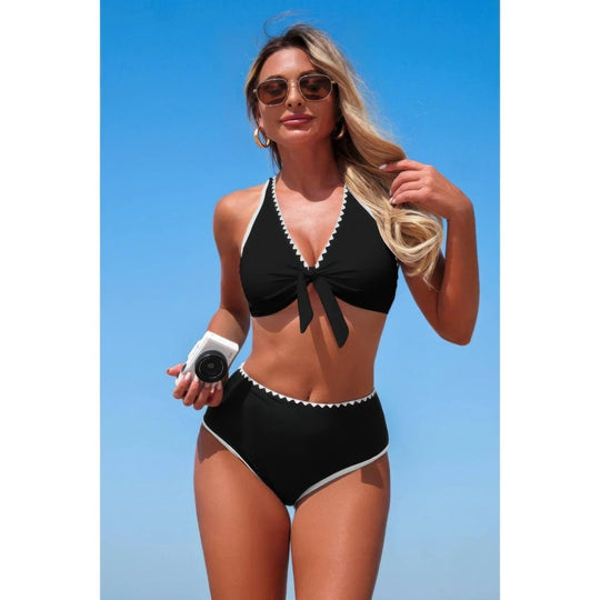 Woman wearing a black bikini with white trim against a blue sky.
