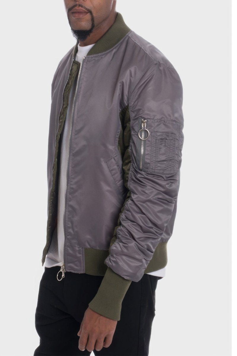 Person wearing a gray bomber jacket with green accents on a white background