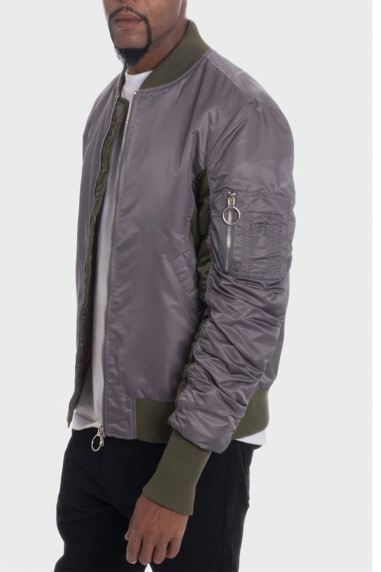 Person wearing a gray bomber jacket with green accents on a white background